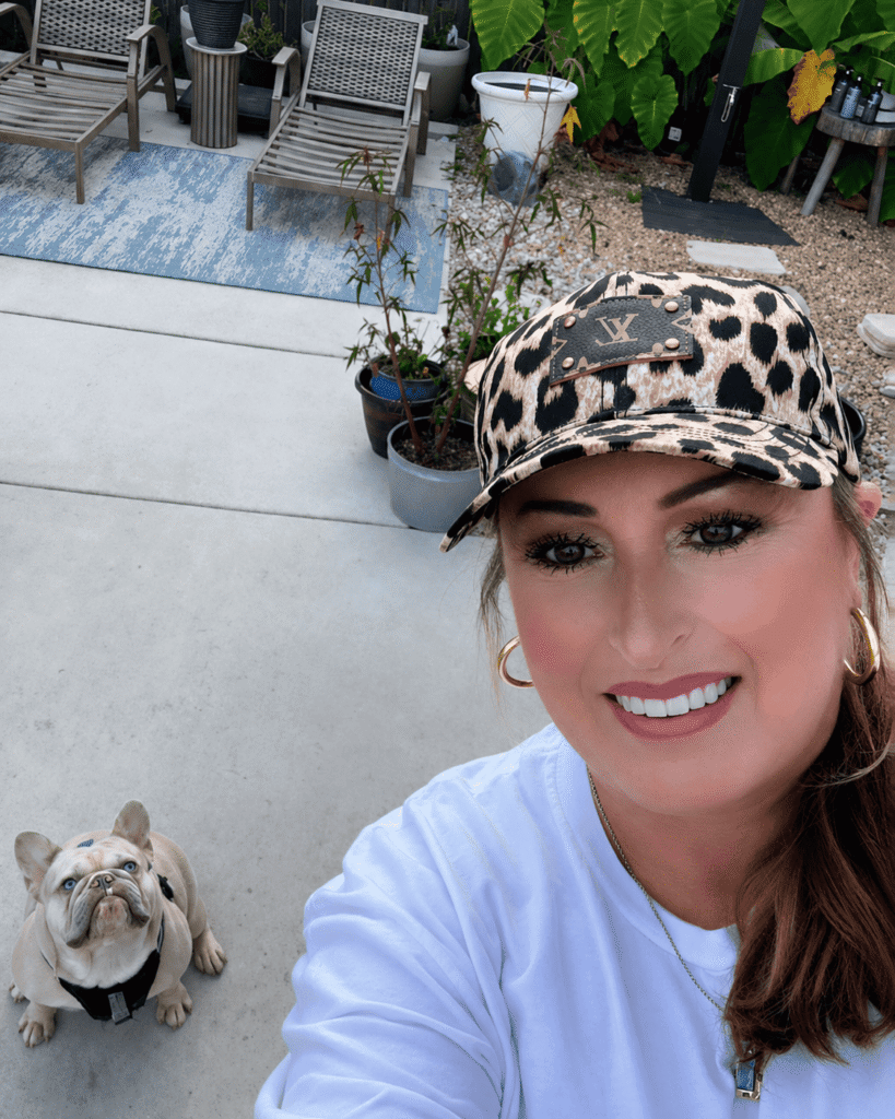 Crissie Willoughby Benoit outdoors at home with one of her French Bulldogs behind her